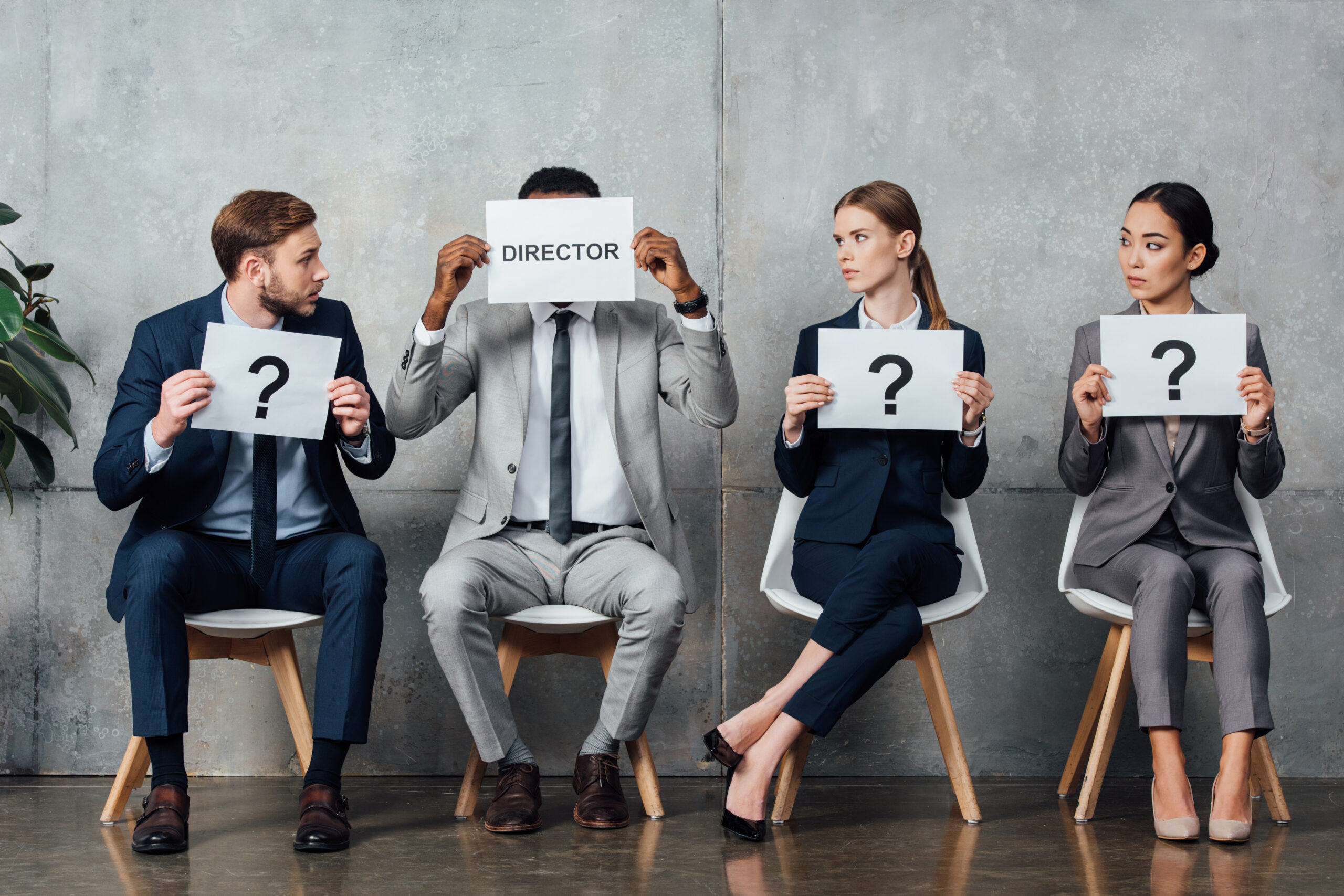 multiethnic businesspeople holding cards with 'director' word and question marks in front of faces in waiting hall